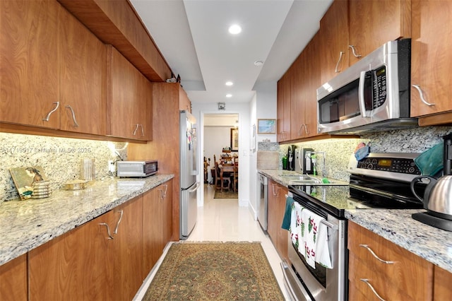 kitchen with sink, stainless steel appliances, decorative backsplash, and light stone countertops