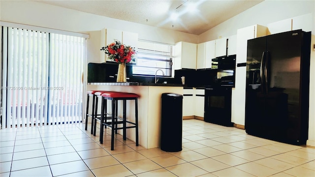 kitchen featuring white cabinets, vaulted ceiling, light tile patterned flooring, a kitchen breakfast bar, and black appliances