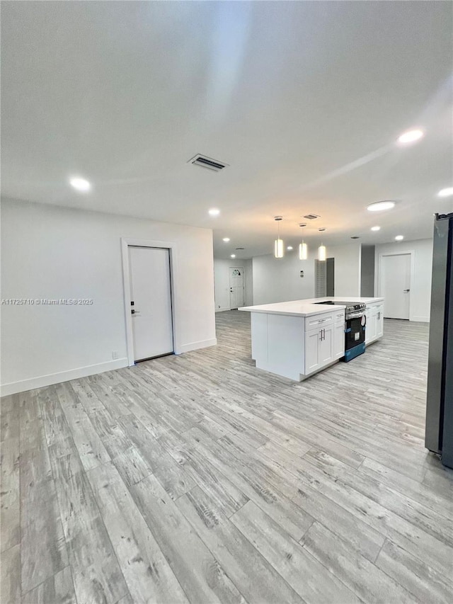 kitchen featuring pendant lighting, white cabinets, appliances with stainless steel finishes, a kitchen island, and light hardwood / wood-style flooring