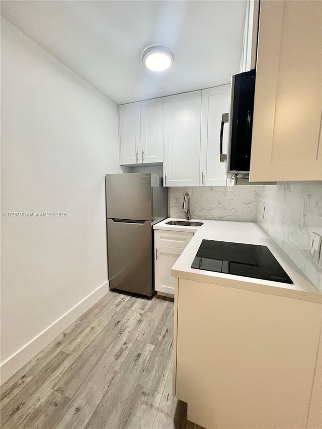 kitchen featuring sink, black electric stovetop, stainless steel fridge, and white cabinetry