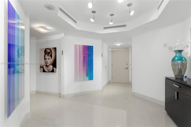 hallway with light tile patterned floors and a tray ceiling