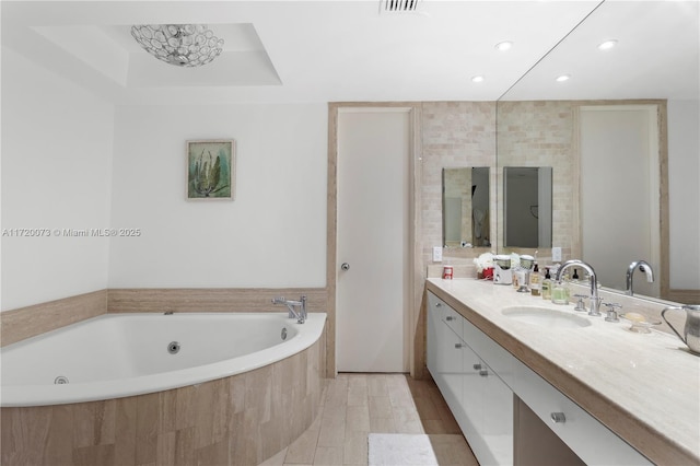 bathroom featuring a relaxing tiled tub, vanity, and a tray ceiling