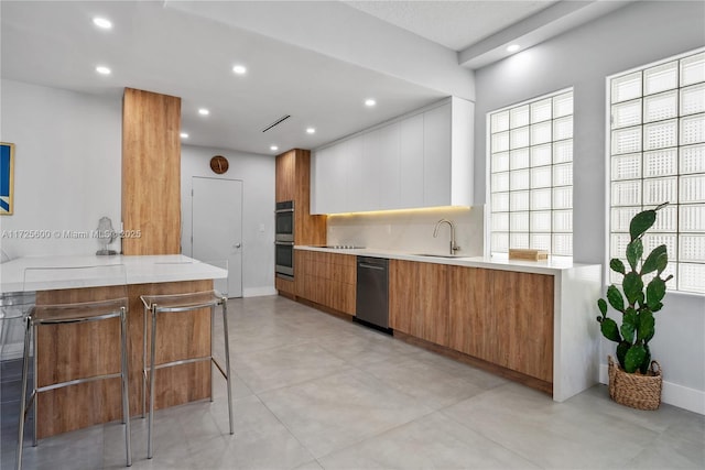 kitchen featuring kitchen peninsula, a breakfast bar, white cabinetry, appliances with stainless steel finishes, and sink