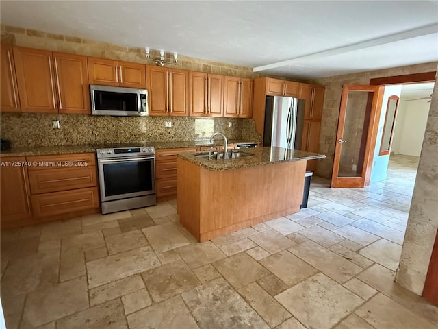 kitchen with dark stone countertops, stone tile flooring, decorative backsplash, stainless steel appliances, and a sink