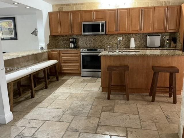 kitchen with appliances with stainless steel finishes, kitchen peninsula, light stone countertops, a breakfast bar, and sink