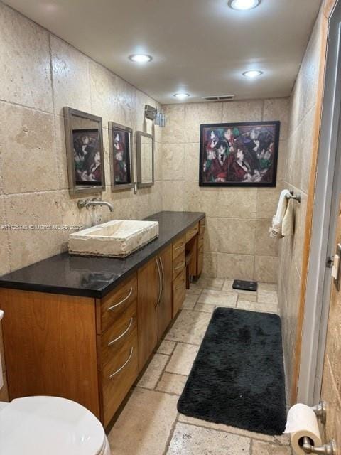 bathroom with toilet, vanity, and tile walls