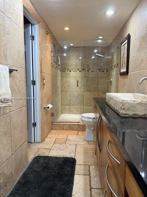 bathroom featuring toilet, a tile shower, tile walls, and vanity