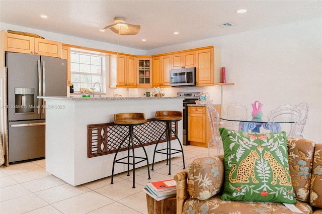 kitchen with light tile patterned floors, light stone countertops, light brown cabinets, and appliances with stainless steel finishes