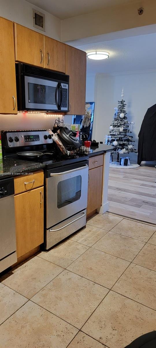 kitchen featuring stainless steel appliances, light tile patterned flooring, and dark stone countertops