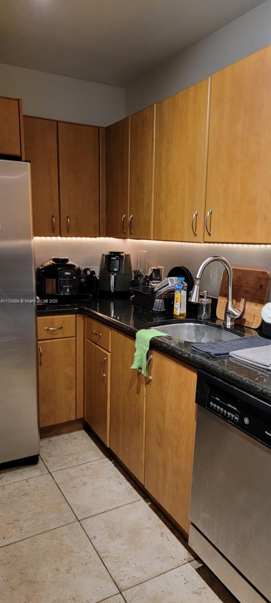 kitchen with stainless steel appliances, dark stone counters, light tile patterned floors, and sink