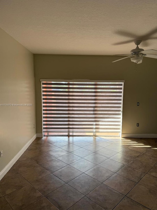 spare room featuring dark tile patterned flooring, a textured ceiling, and a healthy amount of sunlight