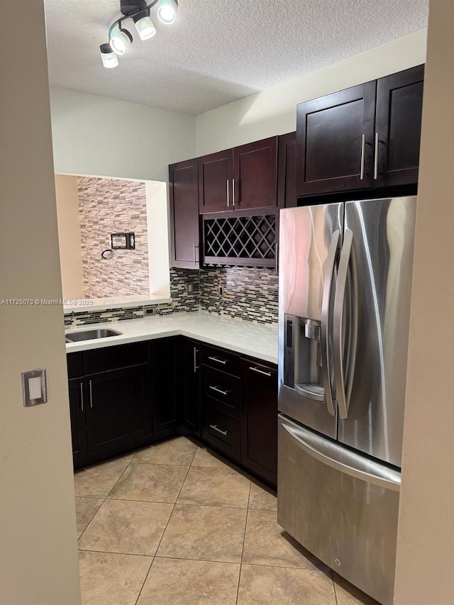 kitchen featuring sink, stainless steel fridge with ice dispenser, a textured ceiling, light tile patterned floors, and backsplash