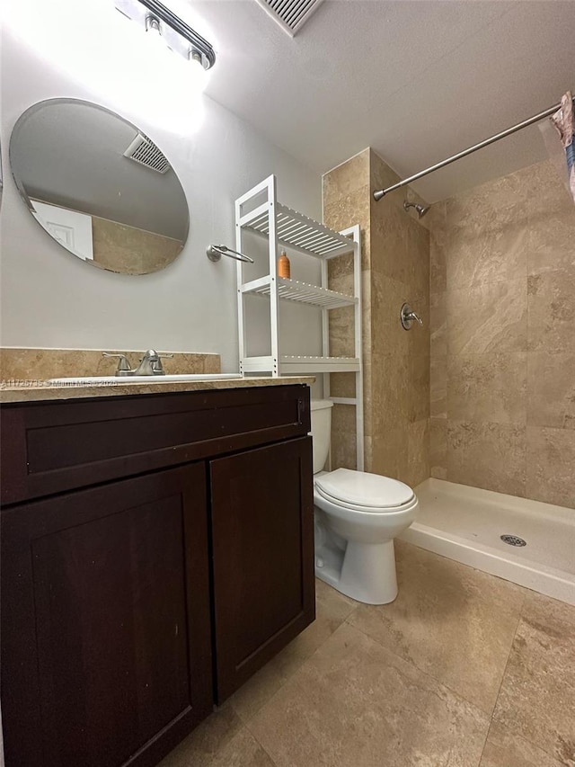 bathroom featuring toilet, tiled shower, and vanity