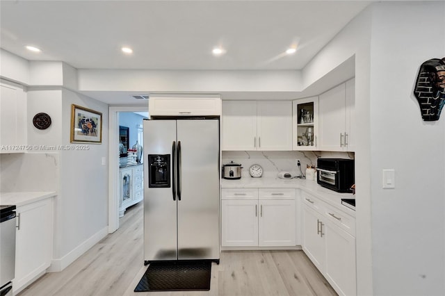 kitchen featuring tasteful backsplash, white cabinetry, stainless steel fridge, and light wood-type flooring