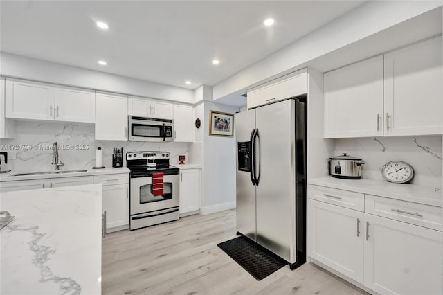 kitchen with sink, appliances with stainless steel finishes, light stone counters, white cabinets, and light wood-type flooring