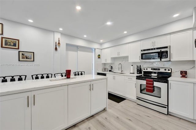 kitchen with tasteful backsplash, sink, white cabinets, stainless steel appliances, and light stone countertops