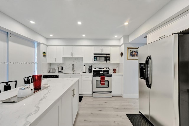 kitchen with appliances with stainless steel finishes, white cabinetry, sink, backsplash, and light stone countertops