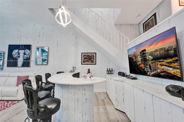 bar with wooden walls, white cabinets, light hardwood / wood-style floors, and decorative light fixtures