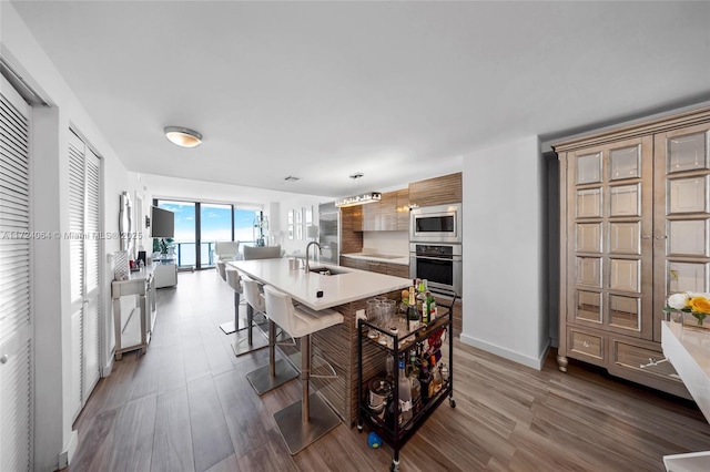 kitchen with a kitchen island with sink, stainless steel appliances, hanging light fixtures, a breakfast bar, and sink