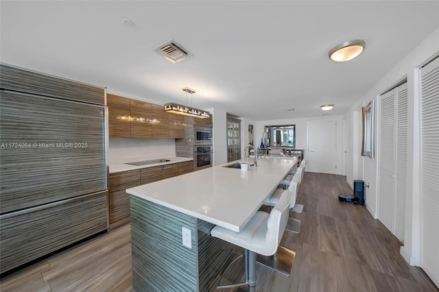 kitchen featuring sink, pendant lighting, a breakfast bar area, a kitchen island with sink, and appliances with stainless steel finishes