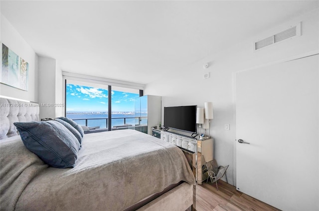 bedroom with hardwood / wood-style floors, expansive windows, and access to exterior