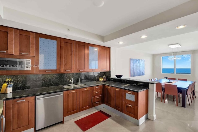 kitchen featuring sink, dark stone countertops, kitchen peninsula, stainless steel appliances, and decorative backsplash