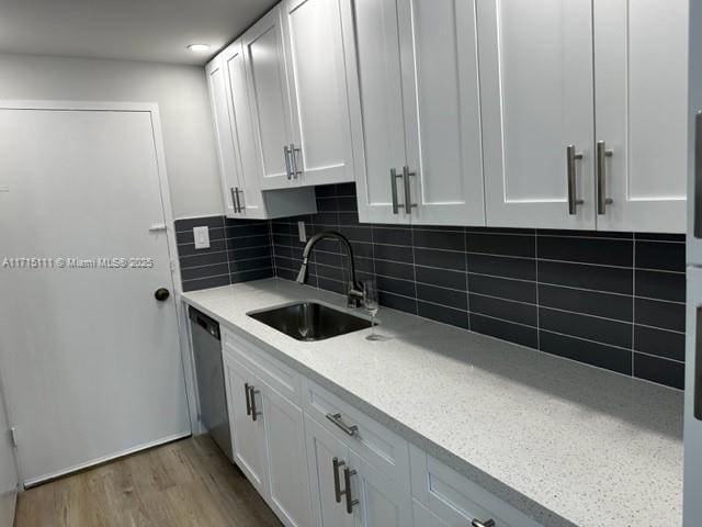 kitchen featuring light stone counters, stainless steel dishwasher, tasteful backsplash, white cabinetry, and sink