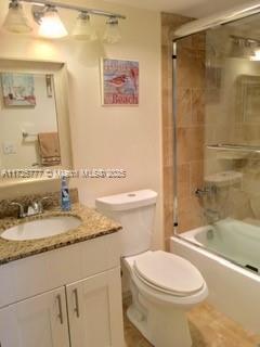 full bathroom with bath / shower combo with glass door, toilet, and vanity