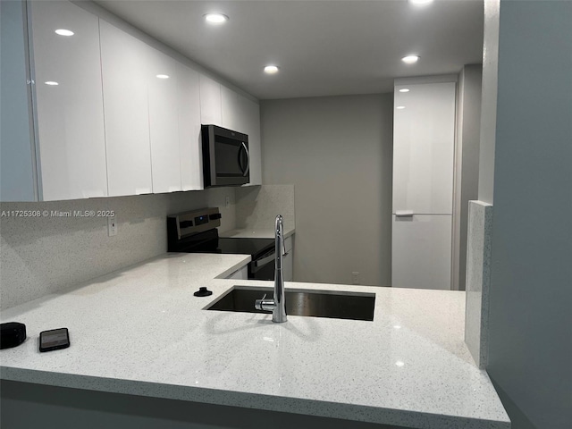 kitchen featuring light stone counters, stainless steel range with electric stovetop, sink, white cabinetry, and tasteful backsplash