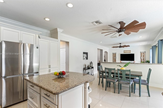 kitchen featuring stone counters, stainless steel refrigerator, white cabinetry, ornamental molding, and light tile patterned floors