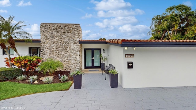 property entrance with a tiled roof, french doors, and stucco siding