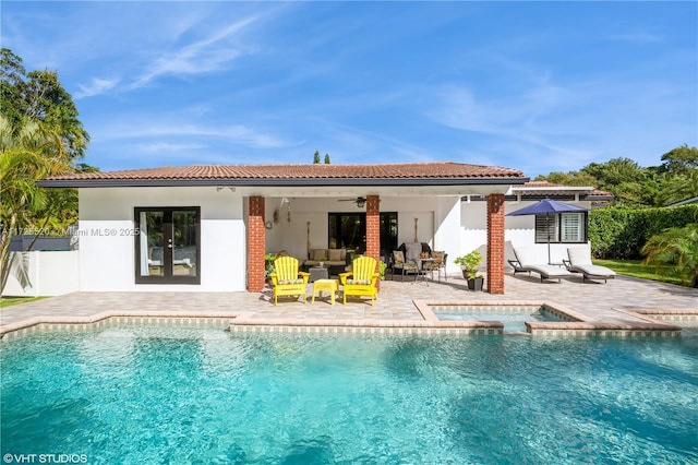 rear view of property featuring ceiling fan, stucco siding, a patio area, an outdoor pool, and an in ground hot tub