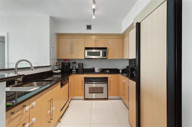 kitchen with sink, light brown cabinets, light tile patterned floors, dark stone counters, and appliances with stainless steel finishes