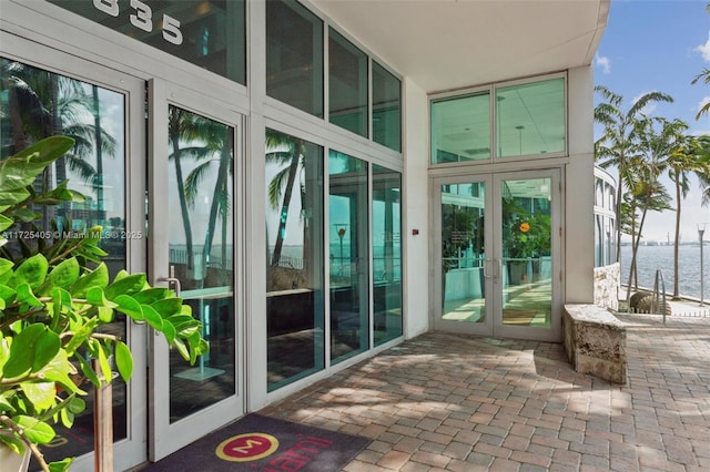 view of exterior entry with french doors, a water view, and a patio area