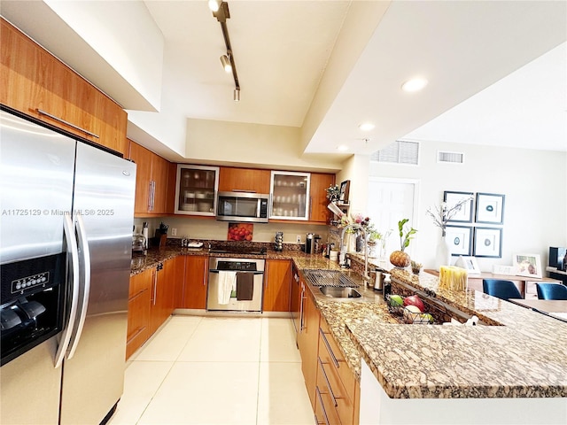 kitchen featuring a peninsula, brown cabinetry, stainless steel appliances, and a sink