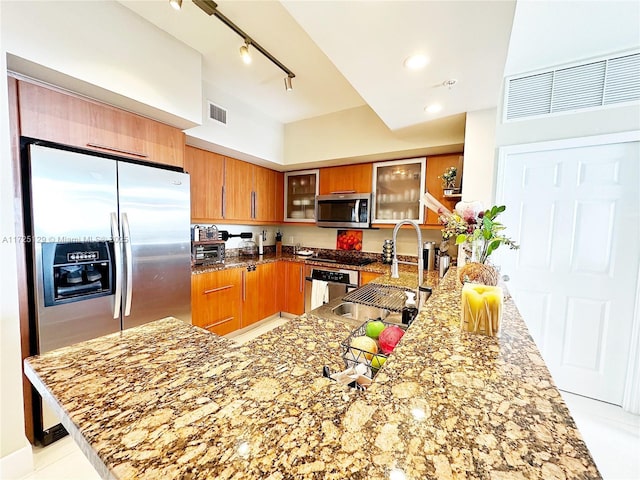 kitchen featuring brown cabinets, stainless steel appliances, visible vents, stone countertops, and a sink