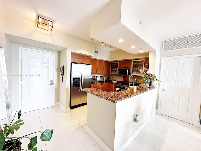 kitchen with light tile patterned floors, a peninsula, appliances with stainless steel finishes, dark stone counters, and glass insert cabinets