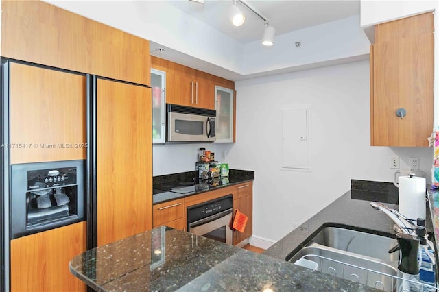 kitchen featuring kitchen peninsula, stainless steel appliances, track lighting, dark stone counters, and sink