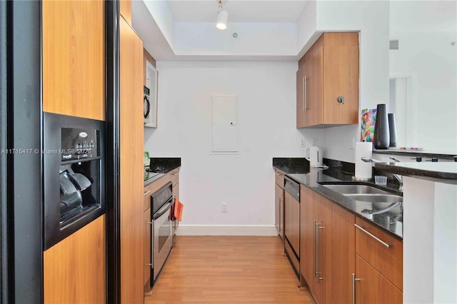 kitchen with sink, electric panel, light hardwood / wood-style floors, dark stone counters, and appliances with stainless steel finishes