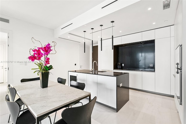 kitchen featuring hanging light fixtures, a breakfast bar, a kitchen island with sink, white cabinetry, and sink