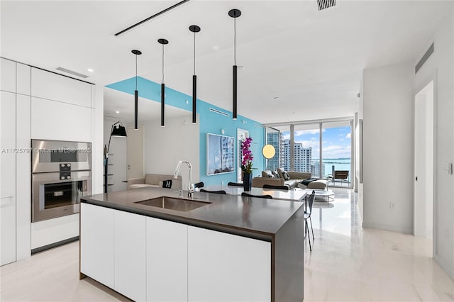 kitchen featuring floor to ceiling windows, white cabinets, pendant lighting, and sink