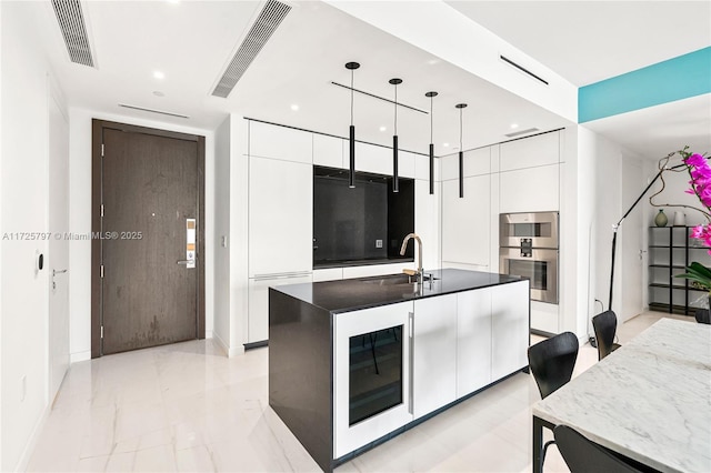 kitchen featuring sink, white cabinets, pendant lighting, double oven, and a kitchen island with sink