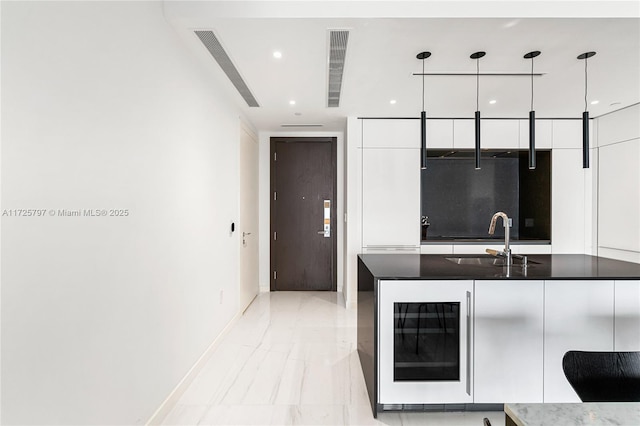 kitchen featuring sink, white cabinets, beverage cooler, and decorative light fixtures