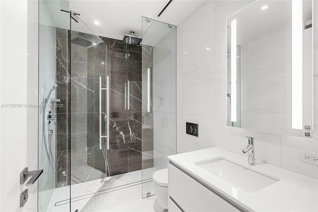 bathroom with tile walls, a shower with door, vanity, and toilet