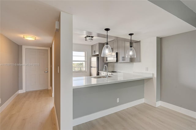 kitchen featuring kitchen peninsula, white refrigerator, pendant lighting, sink, and light hardwood / wood-style flooring