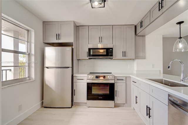 kitchen featuring stainless steel appliances, sink, light hardwood / wood-style floors, hanging light fixtures, and gray cabinetry