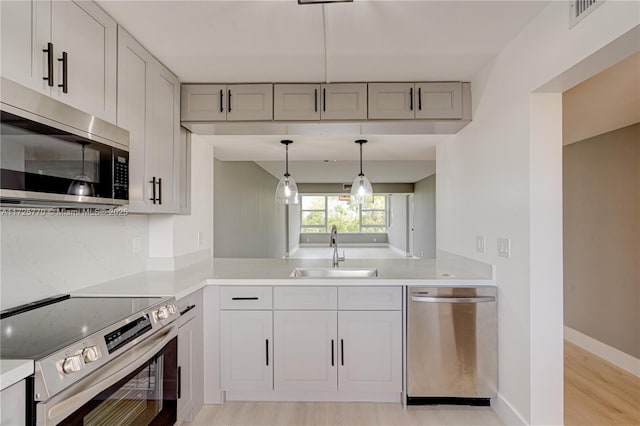 kitchen featuring kitchen peninsula, pendant lighting, stainless steel appliances, light hardwood / wood-style floors, and sink