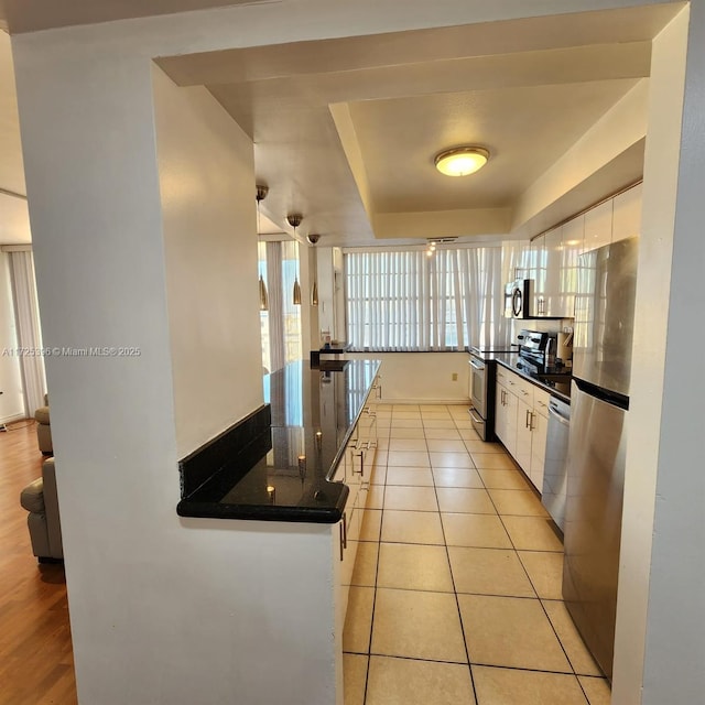 kitchen featuring light tile patterned floors, stainless steel appliances, white cabinetry, and a tray ceiling