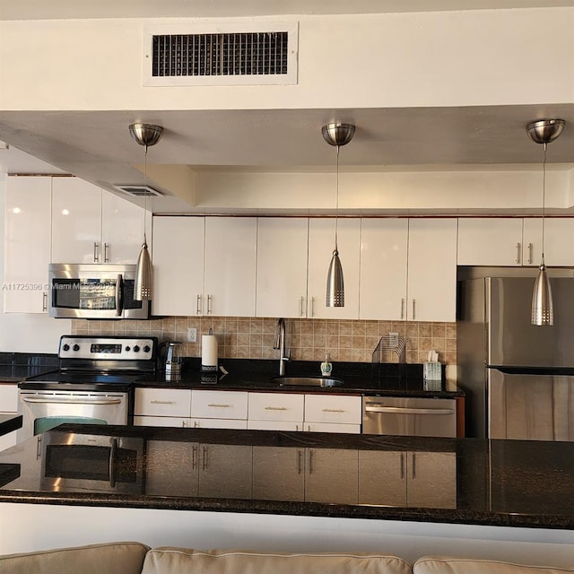 kitchen with appliances with stainless steel finishes, white cabinets, decorative light fixtures, and sink