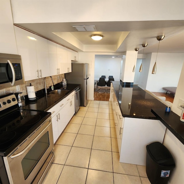 kitchen with appliances with stainless steel finishes, light tile patterned floors, pendant lighting, a tray ceiling, and white cabinets